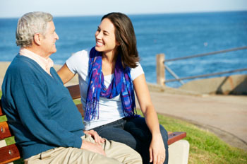 Senior Man Sitting On Bench With Adult Daughter By Sea